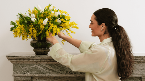Donna che sistema un bouquet di mimosa in vaso decorativo su una mensola in casa