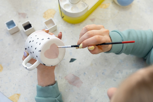 Persona che dipinge un cuore rosa su una tazza bianca personalizzata con un pennello.