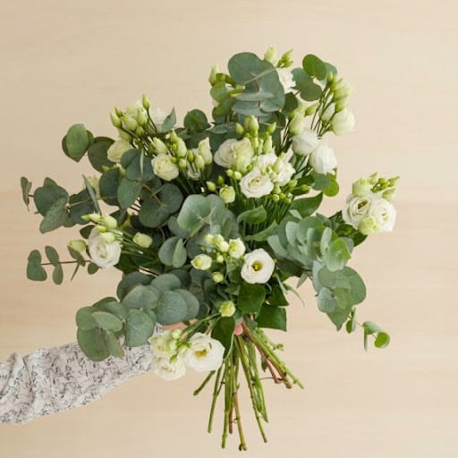 bouquet di lisianthus bianchi tenuti da una mano e decorati con elementi naturali verdi